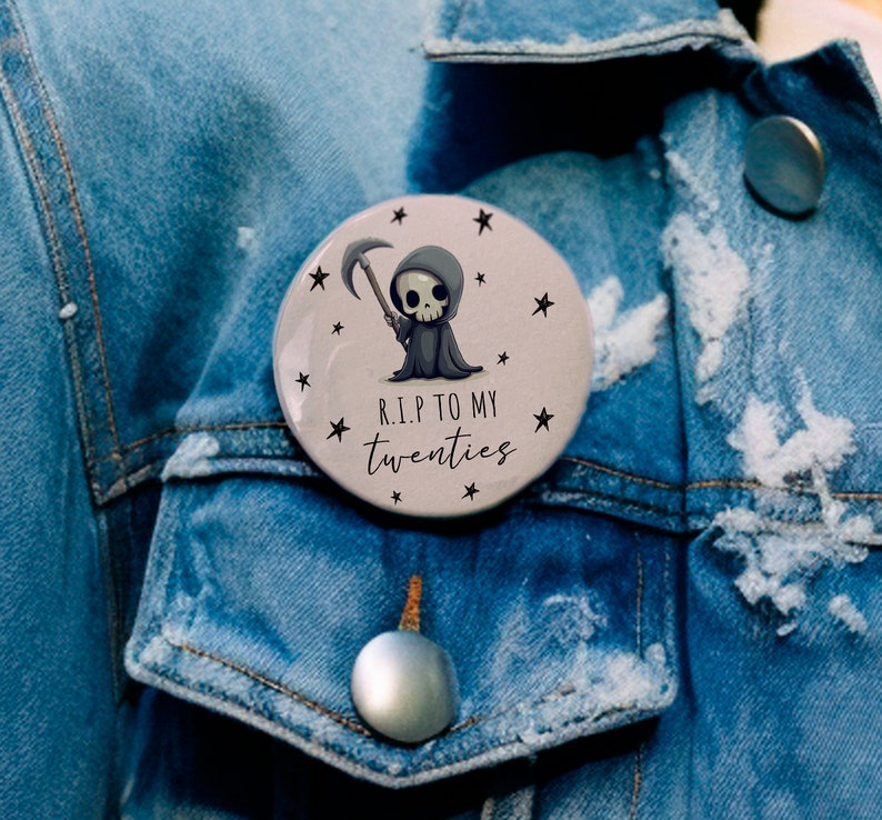 May include: A round button with a cartoon grim reaper holding a scythe. The button has a white background with black stars and the text "R.I.P. TO MY TWENTIES".