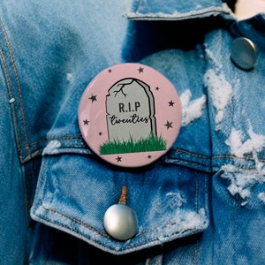 May include: A pink button with a tombstone graphic and the text "R.I.P. twenties" surrounded by stars.