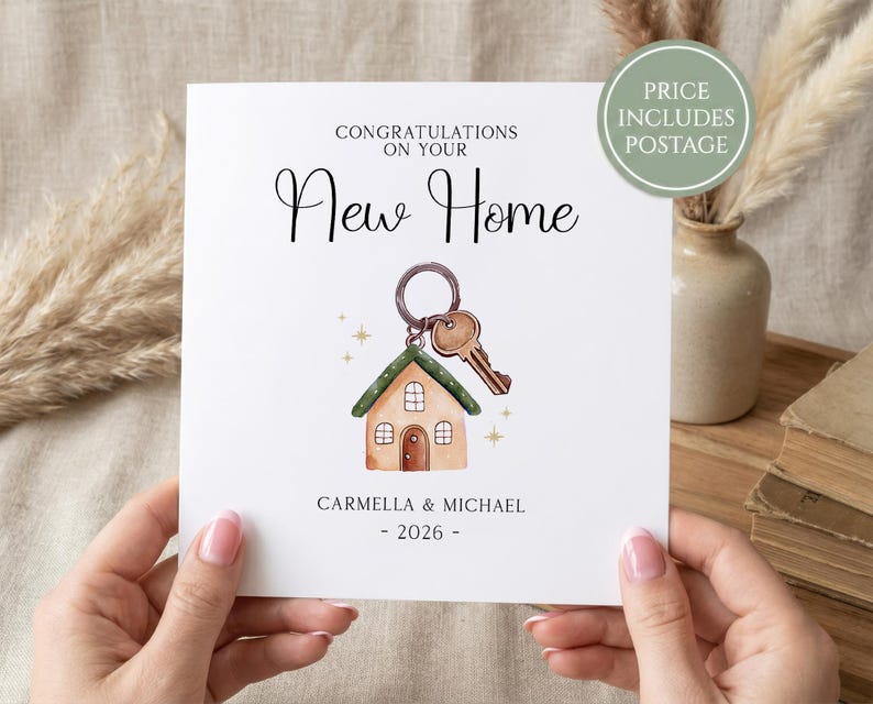 K&ouml;nnte beinhalten: Wei&szlig;e Karte mit dem Text &bdquo;Gl&uuml;ckwunsch zu Ihrem neuen Zuhause&ldquo; und einer Aquarellillustration eines Hauses mit Schl&uuml;sseln. Die Karte enth&auml;lt die Namen Carmella & Michael und das Jahr 2026.