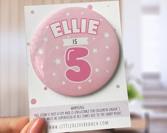 May include: Pink and white round button with the text "Ellie is 5" and white stars. The button has a warning that it is not a toy and is unsuitable for children under 3.