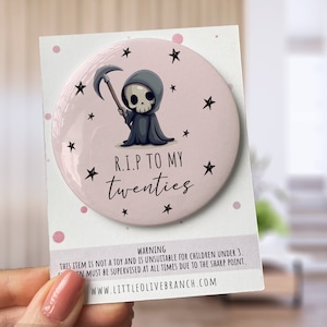 May include: A pink round button with a cartoon grim reaper holding a scythe. The button has black stars and the text "R.I.P TO MY twenties".