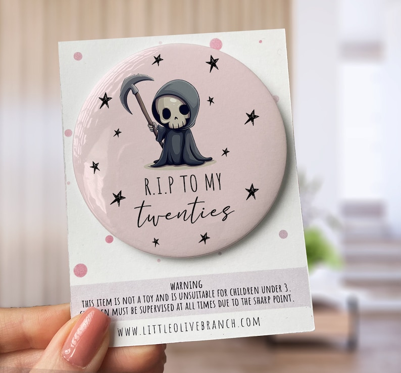 May include: A pink round button with a cartoon grim reaper holding a scythe. The button has black stars and the text "R.I.P TO MY twenties".