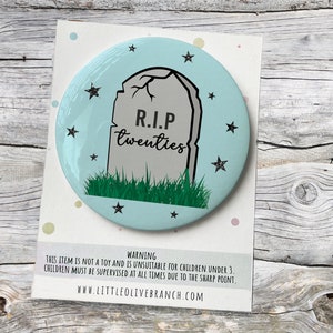 May include: A light blue round button with a black and white illustration of a tombstone with the text "R.I.P twenties" on it. The tombstone is surrounded by green grass and black stars.