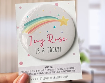 Könnte beinhalten: Ein weißer runder Knopf mit einem Regenbogen-Sternschnuppen-Design und dem Text "Ivy Rose ist 6 heute!" in rosa Schrift. Der Knopf hat einen weißen Hintergrund mit rosa Punkten.