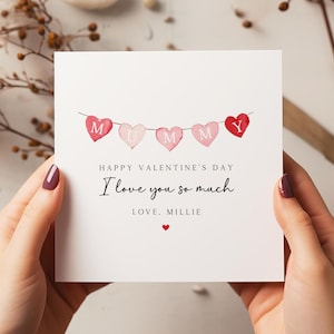 May include: A white card with a pink and red watercolour illustration of a string of hearts with the word "MUMMY" spelled out. The card reads "Happy Valentine's Day I love you so much Love, Millie".