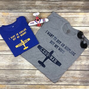 Peut inclure: Un t-shirt bleu avec le texte jaune I WANT AN AIRPLANE BUT MY MOMMY et un graphique d'avion jaune marqu&eacute; CESS-NAH, &agrave; c&ocirc;t&eacute; d'un t-shirt gris avec le texte noir I WANT TO BUY AN AIRPLANE BUT MY WIFE et un graphique d'avion noir.
