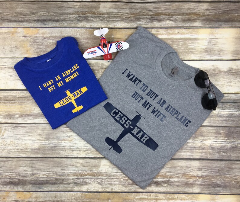 Peut inclure: Un t-shirt bleu avec le texte jaune I WANT AN AIRPLANE BUT MY MOMMY et un graphique d'avion jaune marqu&eacute; CESS-NAH, &agrave; c&ocirc;t&eacute; d'un t-shirt gris avec le texte noir I WANT TO BUY AN AIRPLANE BUT MY WIFE et un graphique d'avion noir.