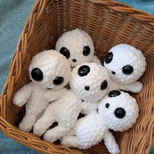 May include: A wicker basket filled with five white crocheted plush toys. Each toy has large black eyes and a simple, round face.