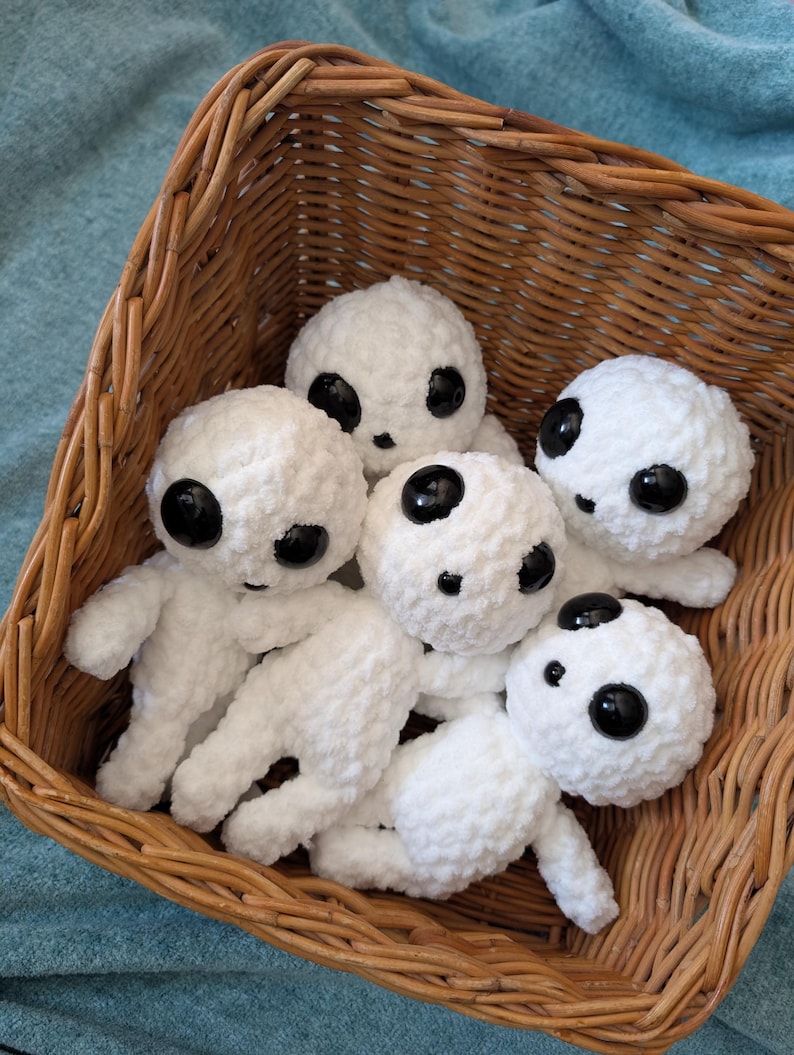 May include: A wicker basket filled with five white crocheted plush toys. Each toy has large black eyes and a simple, round face.