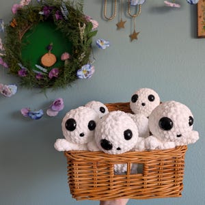 May include: A wicker basket filled with white crocheted plush toys with black eyes. The toys are arranged in a cluster, with some peeking over the edge of the basket.