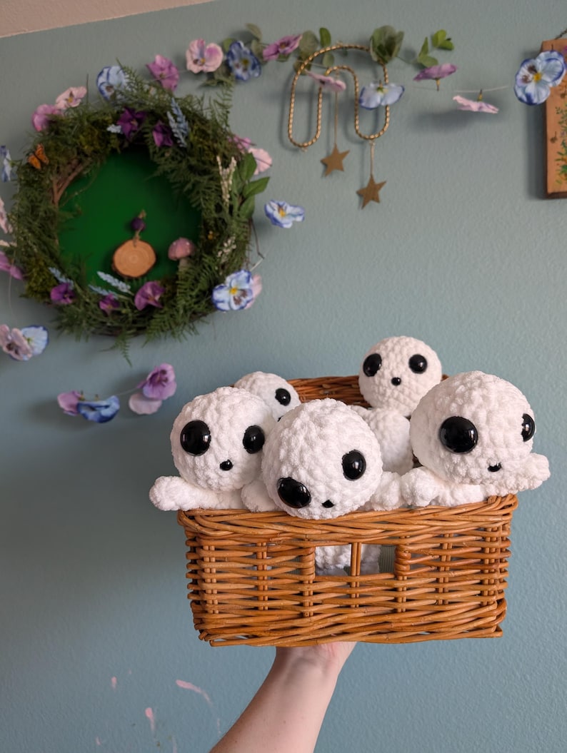 May include: A wicker basket filled with white crocheted plush toys with black eyes. The toys are arranged in a cluster, with some peeking over the edge of the basket.