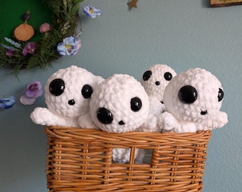 May include: A wicker basket filled with five white crocheted plush toys with black eyes. The toys are arranged in a cluster, with their heads peeking out of the basket.