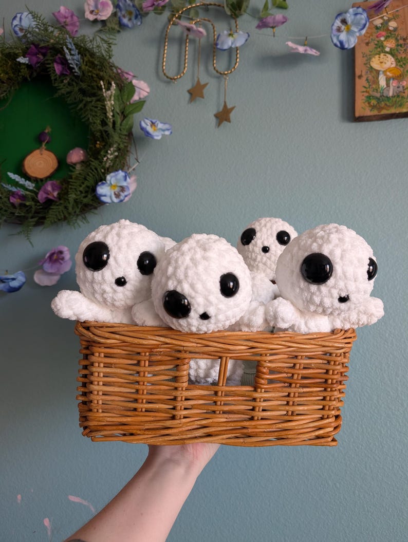 May include: A wicker basket filled with five white crocheted plush toys with black eyes. The toys are arranged in a cluster, with their heads peeking out of the basket.