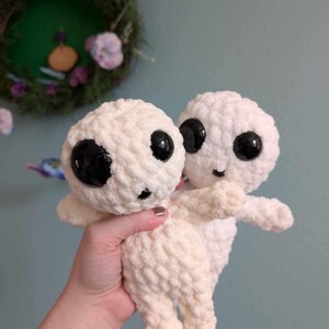May include: Two crocheted plush toys in a cream color with black eyes. The toys are holding onto each other.