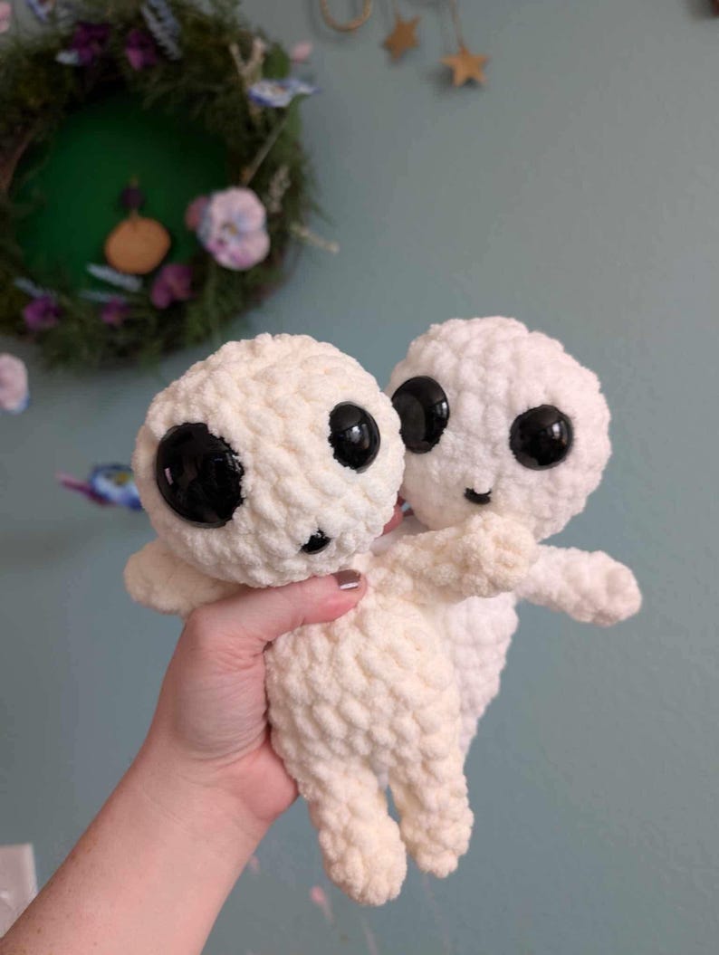 May include: Two crocheted plush toys in a cream color with black eyes. The toys are holding onto each other.