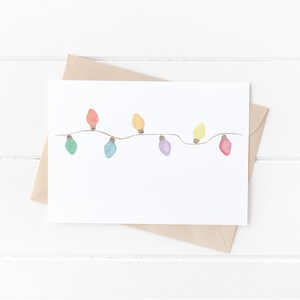 Op de afbeelding: Een witte kaart met een string van kleurrijke lampjes die erop getekend zijn. De lampjes zijn rood, oranje, geel, groen, blauw, paars en roze.