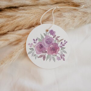 May include: A round white tag with a watercolor illustration of a bouquet of purple roses and green leaves.