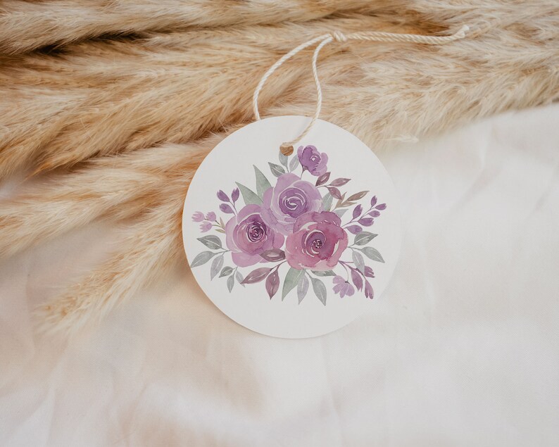 May include: A round white tag with a watercolor illustration of a bouquet of purple roses and green leaves.