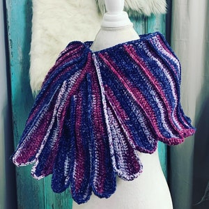 May include: A purple and blue crocheted shawl with a scalloped edge. The shawl is draped over a white mannequin.