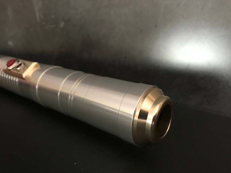 May include: A silver lightsaber with a gold-colored tip and a red button on the side.
