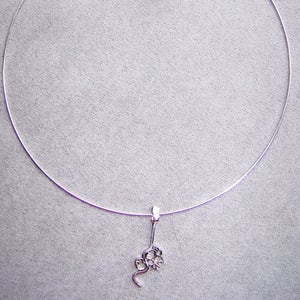 Op de afbeelding: Een zilveren ketting met een delicate slangenhanger. De slang is opgerold met zijn staart in zijn mond, en heeft een klein bloemetjesontwerp op zijn kop.