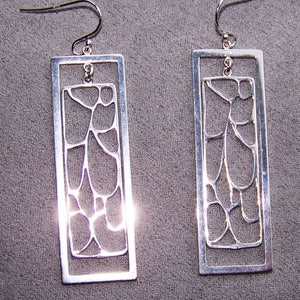May include: A pair of silver-toned rectangular drop earrings. Each earring features an outer rectangular frame with an inner, abstract design. The inner design has an open, organic pattern. The earrings hang from a curved ear wire.