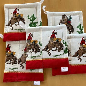 May include: Set of five white cotton pot holders with red trim. Each pot holder features a colorful illustration of a cowboy riding a horse with a cactus in the background.