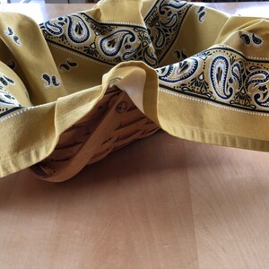 May include: A yellow bandana with a black and white paisley pattern is draped over a woven basket.