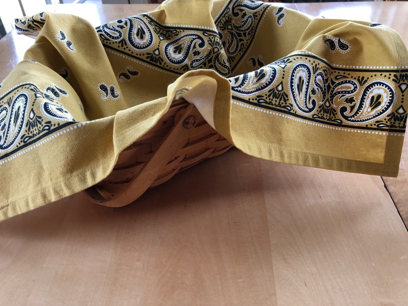 May include: A yellow bandana with a black and white paisley pattern is draped over a woven basket.