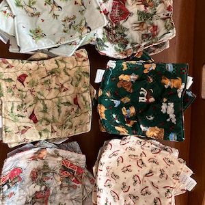 May include: A collection of bowl cozies with various holiday-themed patterns. Designs include birds on branches, cardinals, farm scenes, dogs, and rocking horses. The cozies are made of fabric and are in shades of green, beige, and white.