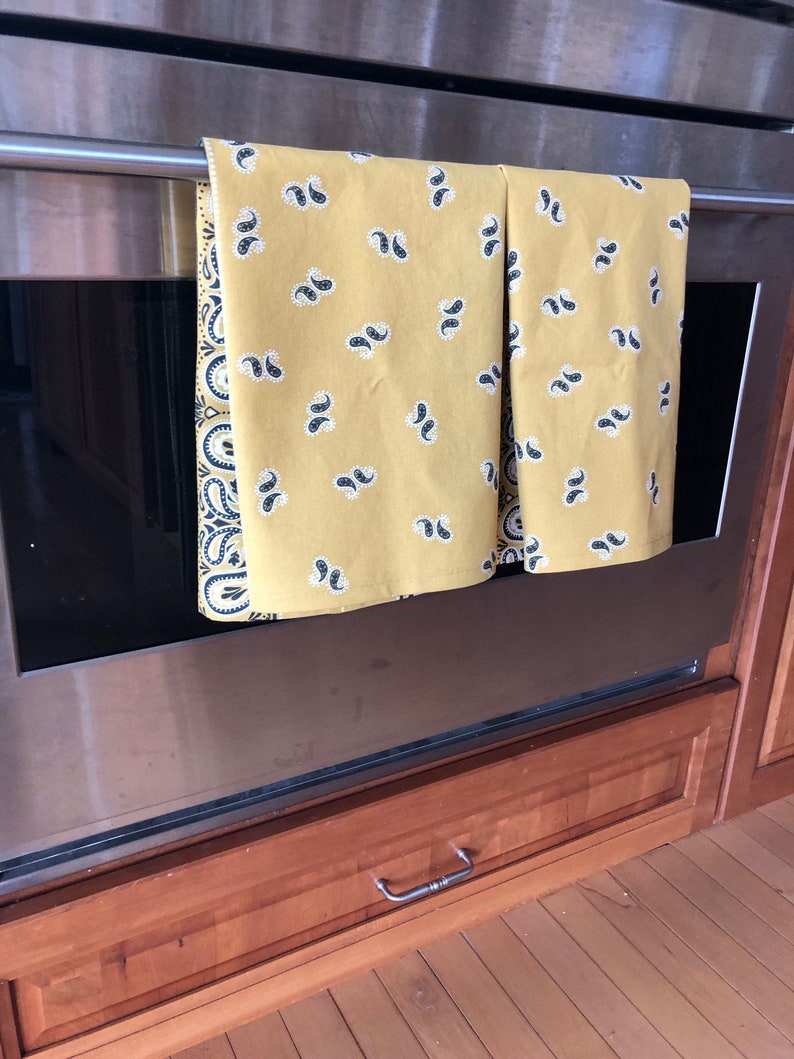 May include: Two yellow kitchen towels with a paisley pattern hang on a silver oven rack.