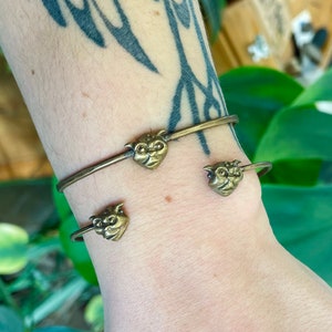 Könnte beinhalten: Drei goldfarbene Armbänder mit einem Cartoon-Gesichtsanhänger an jedem. Die Anhänger sind alle unterschiedlich, aber sie haben alle die gleiche Grundform.