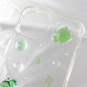 May include: A clear phone case with a green turtle, green four-leaf clovers, and green bubbles embedded inside.