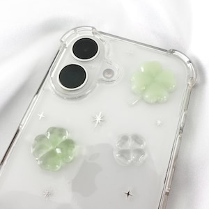 May include: Clear phone case with a design of four-leaf clovers. The clovers are made of a translucent green material and are raised from the case. The case also has a silver glitter design.