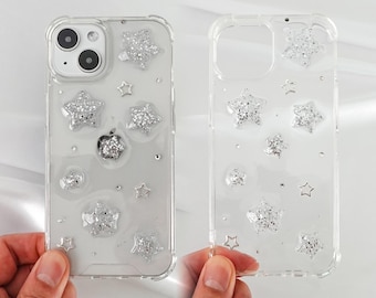 May include: A clear phone case with a glittery star design. The case is made of a clear plastic material and has a raised edge around the camera lens.