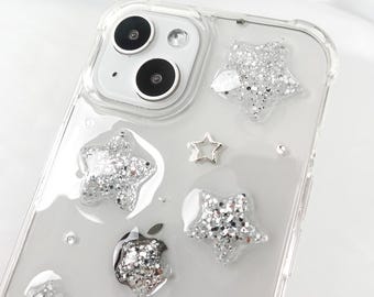 May include: A clear phone case with a glittery star design. The case has a cutout for the camera lens and a small silver star charm.