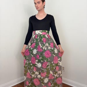 May include: A black long-sleeved top and a floral maxi skirt. The skirt has large pink flowers, white details, and green leaves on a black and white checkered pattern. The skirt extends to the floor.