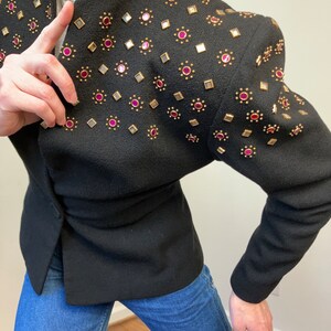 May include: A black blazer with gold and pink embellishments. The blazer has a fitted silhouette and a pointed collar.