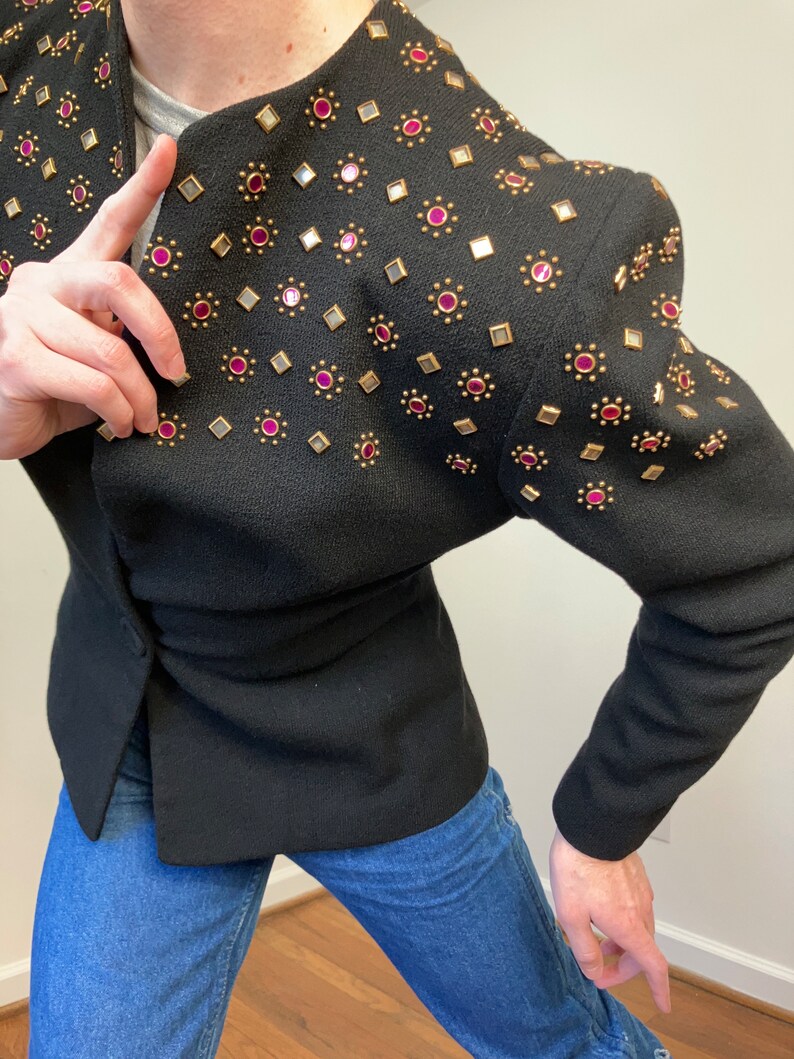 May include: A black blazer with gold and pink embellishments. The blazer has a fitted silhouette and a pointed collar.