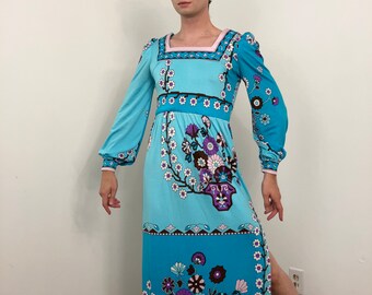May include: A vintage maxi dress in shades of turquoise and teal, featuring a square neckline and long, flowing sleeves. The dress is adorned with a floral pattern in purple, brown, and white, and has a high side slit. The dress has a pink trim.