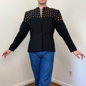 May include: A black blazer with a single button closure and a unique design featuring gold and pink embellishments on the shoulders.
