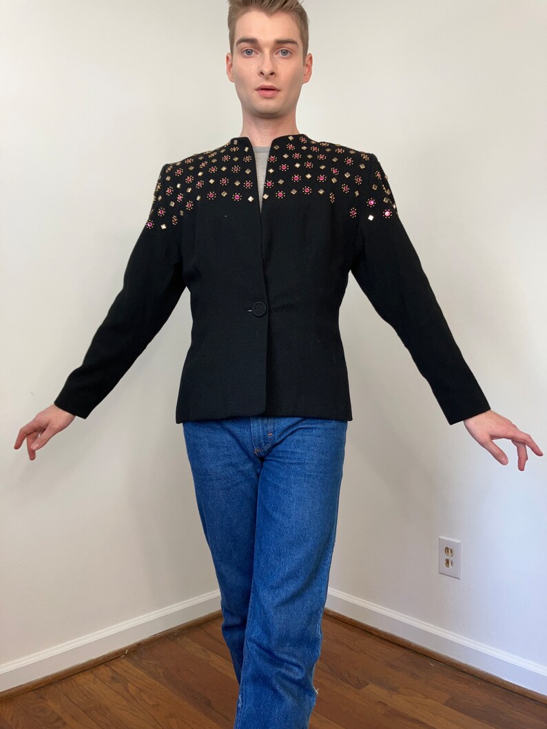 May include: A black blazer with a single button closure and a unique design featuring gold and pink embellishments on the shoulders.