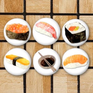 May include: A set of six circular buttons featuring illustrations of various sushi pieces, including salmon roe, shrimp, a maki roll, tamago, a small bowl of soy sauce with chopsticks, and a piece of salmon nigiri on a white background.