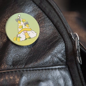 K&ouml;nnte beinhalten: Ein gelber und gr&uuml;ner Knopf mit einem Comic-Zwerg, der einen Hut mit Zitronen und einen wei&szlig;en Bart tr&auml;gt. Der Zwerg ist von Zitronen umgeben.