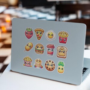 Pu&ograve; includere: Un computer portatile con una variet&agrave; di adesivi colorati che raffigurano cibi di cartoni animati, tra cui una fragola, una pizza, un uovo, patatine fritte, un corn dog, un hamburger, una tazza di caff&egrave;, toast, popcorn, pancake, un biscotto e un ananas.