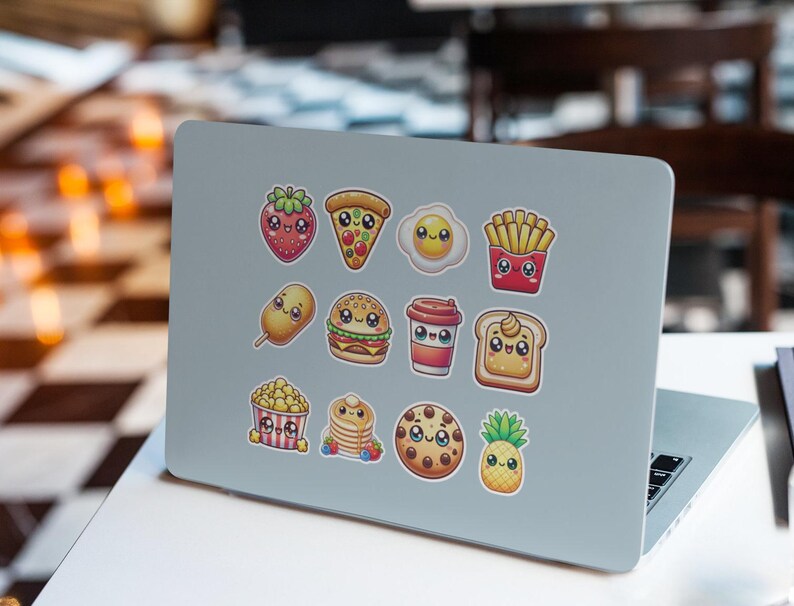 Pu&ograve; includere: Un computer portatile con una variet&agrave; di adesivi colorati che raffigurano cibi di cartoni animati, tra cui una fragola, una pizza, un uovo, patatine fritte, un corn dog, un hamburger, una tazza di caff&egrave;, toast, popcorn, pancake, un biscotto e un ananas.