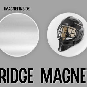 May include: A black and white image of a hockey goalie mask fridge magnet. The magnet is round and has a white background. The text (MAGNET INSIDE) is printed on the top of the magnet. The text FRIDGE MAGNET is printed below the magnet.