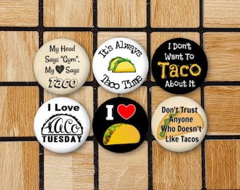 May include: Six round buttons with various taco-themed designs. The buttons feature black and white text and images of tacos on white, black, and cream backgrounds.