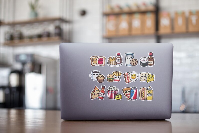 May include: A laptop computer with a variety of colorful stickers depicting cartoon food items, including a slice of pizza, a hot dog, a hamburger, a glass of milk, a donut, a cupcake, a piece of toast, a bottle of ketchup, a bottle of hot sauce, a bag of popcorn, a french fry, a piece of bacon, an egg, a piece of cheese, a piece of sushi, a bottle of syrup, and a glass of milk.