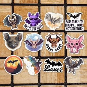 May include: A collection of eleven bat-themed stickers featuring various designs, including a purple bat with sunglasses, a pink bat, a bat silhouette against a moon, and text reading Bat to the Bone, Wanna Hang, and Bats Make Me Happy... You, Not So Much.